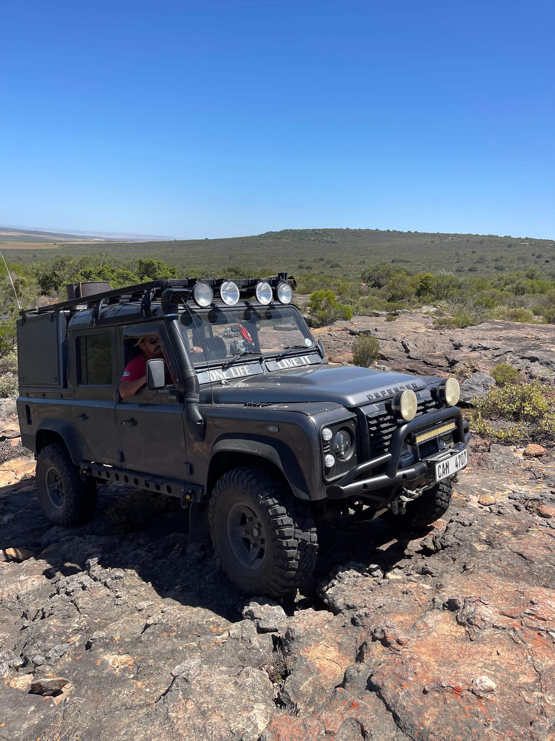 Black Land Rover Defender crossing rocky mountain terrain