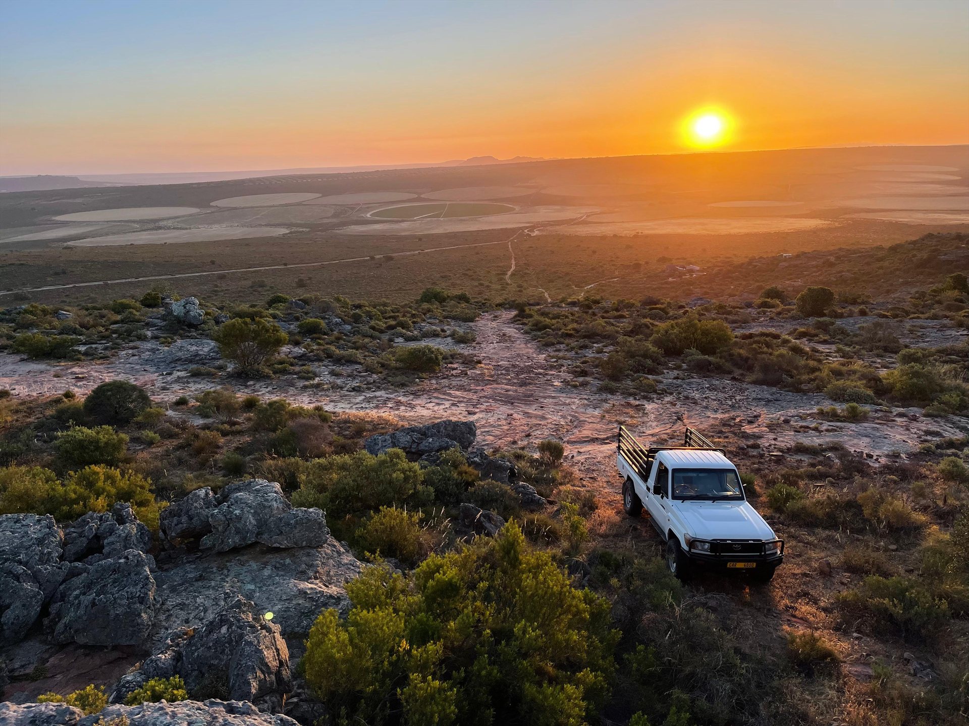 White 4x4 vehicle on a rocky trail overlooking the landscape at sunset