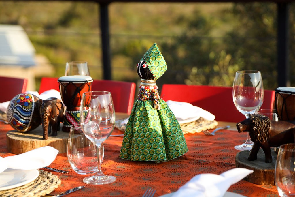 Green fabric doll, small wooden animal figures, drums and glassware on a decorated table