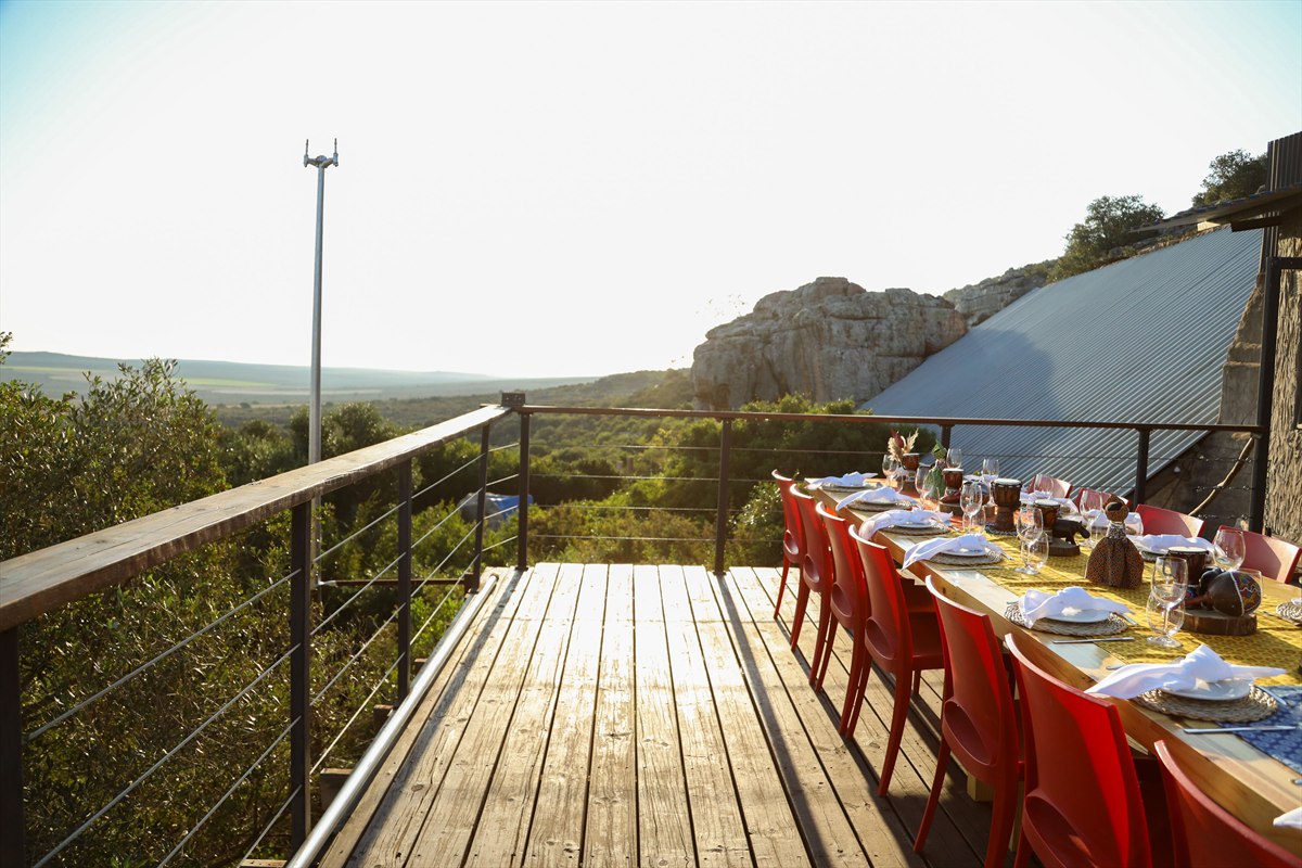 Outdoor dining table set with white napkins and red chairs on a wooden deck beside rock formations