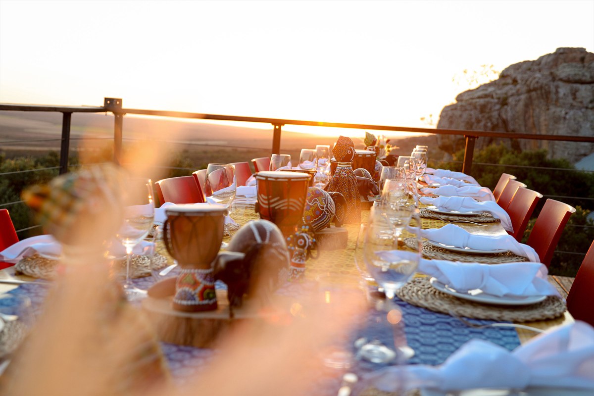 Long outdoor dining table with red chairs and white napkins in the light of the setting sun