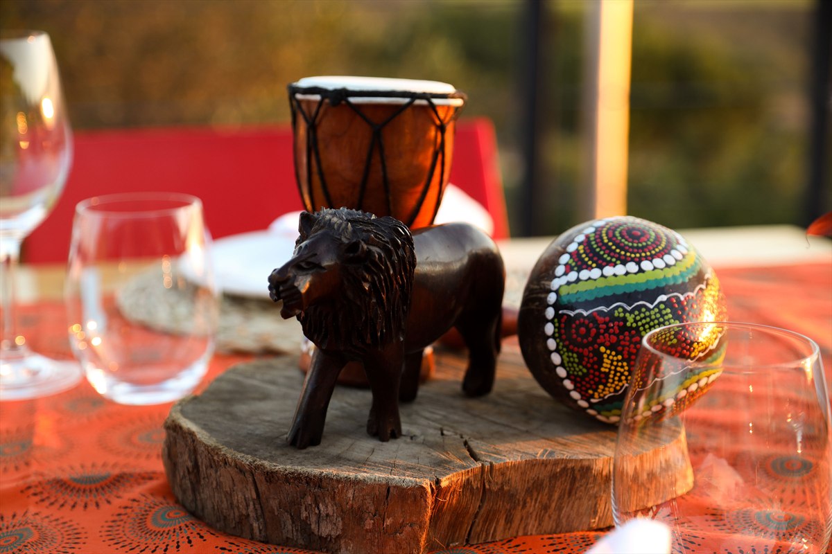 Small wooden lion, painted ornament and hand drum arranged among wine glasses on a table