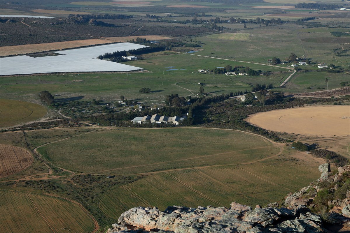 Wide view from a rocky hillside across farmland, roads and greenhouse structures near Donkieskraal