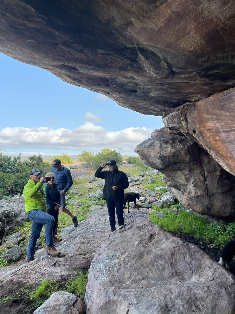 Visitors and dogs gathered beneath a large sandstone overhang at Donkieskraal