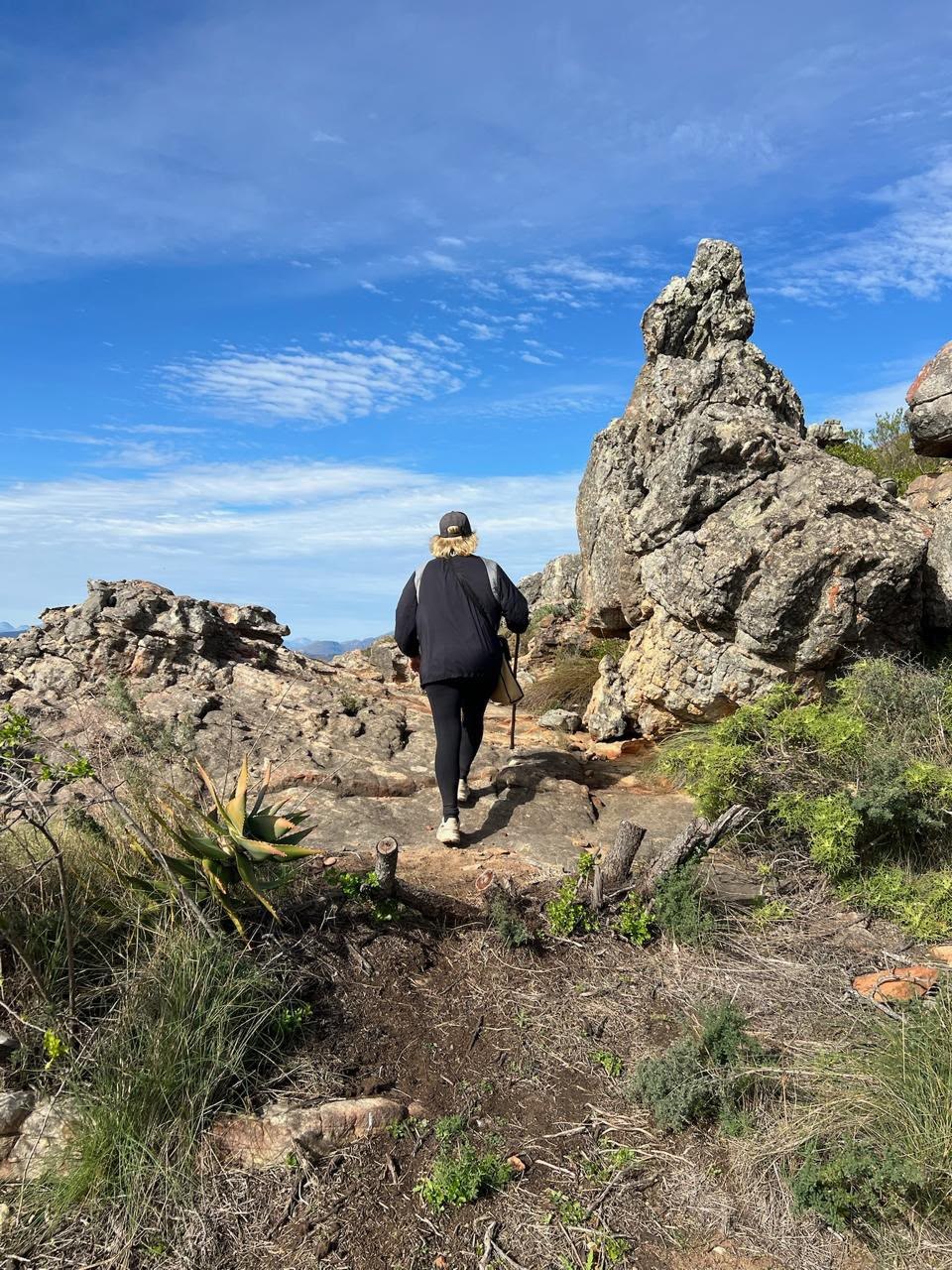 Hiker walking between rugged rock formations under a blue sky at Donkieskraal