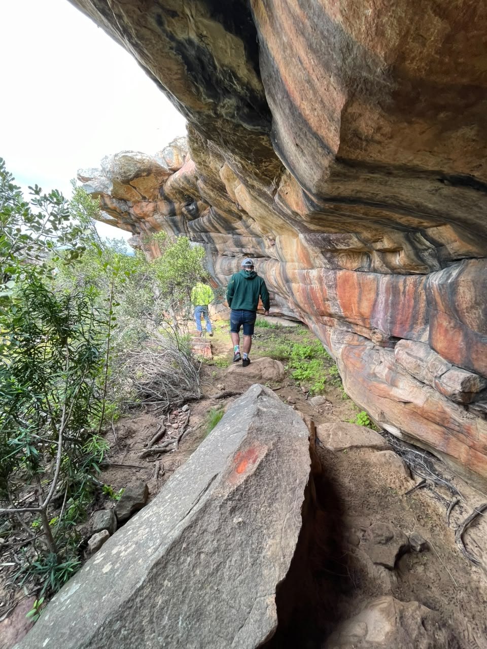 Two hikers walking beside a striped sandstone wall at Donkieskraal