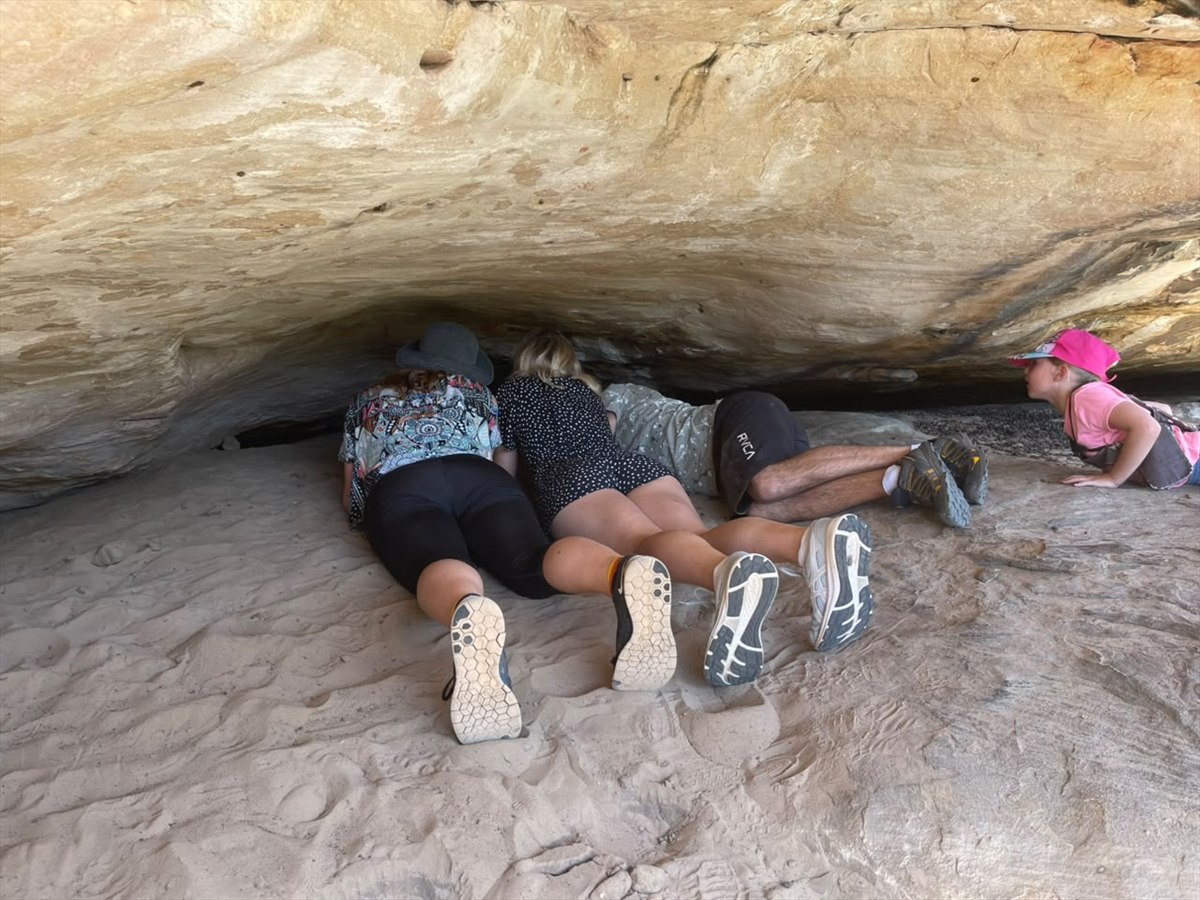 Visitors lying beneath a low sandstone overhang to look into a rock crevice at Donkieskraal
