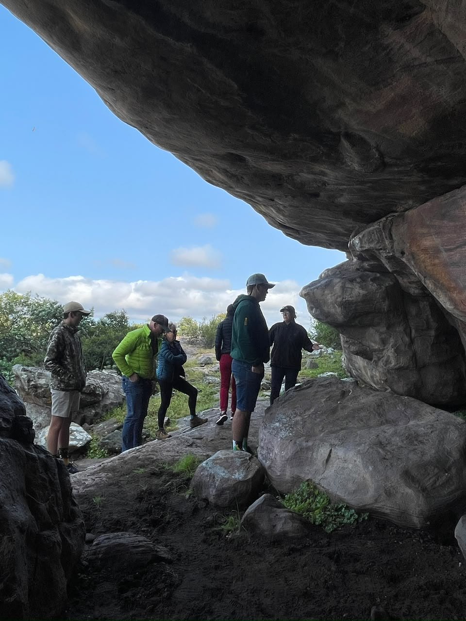 Visitors standing among boulders beneath a sandstone shelter at Donkieskraal