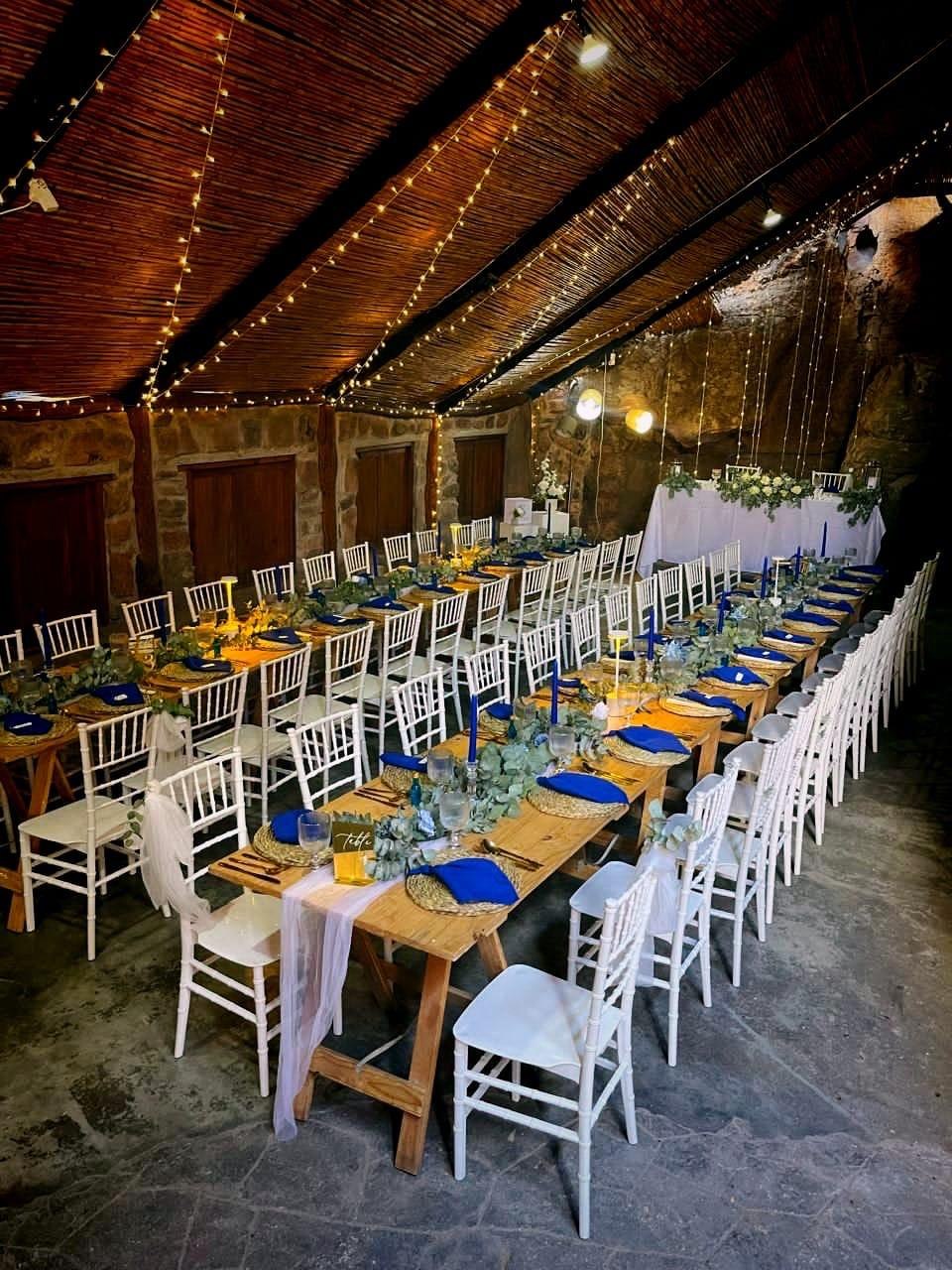 Long wooden wedding tables with blue place settings inside the Donkieskraal rock venue